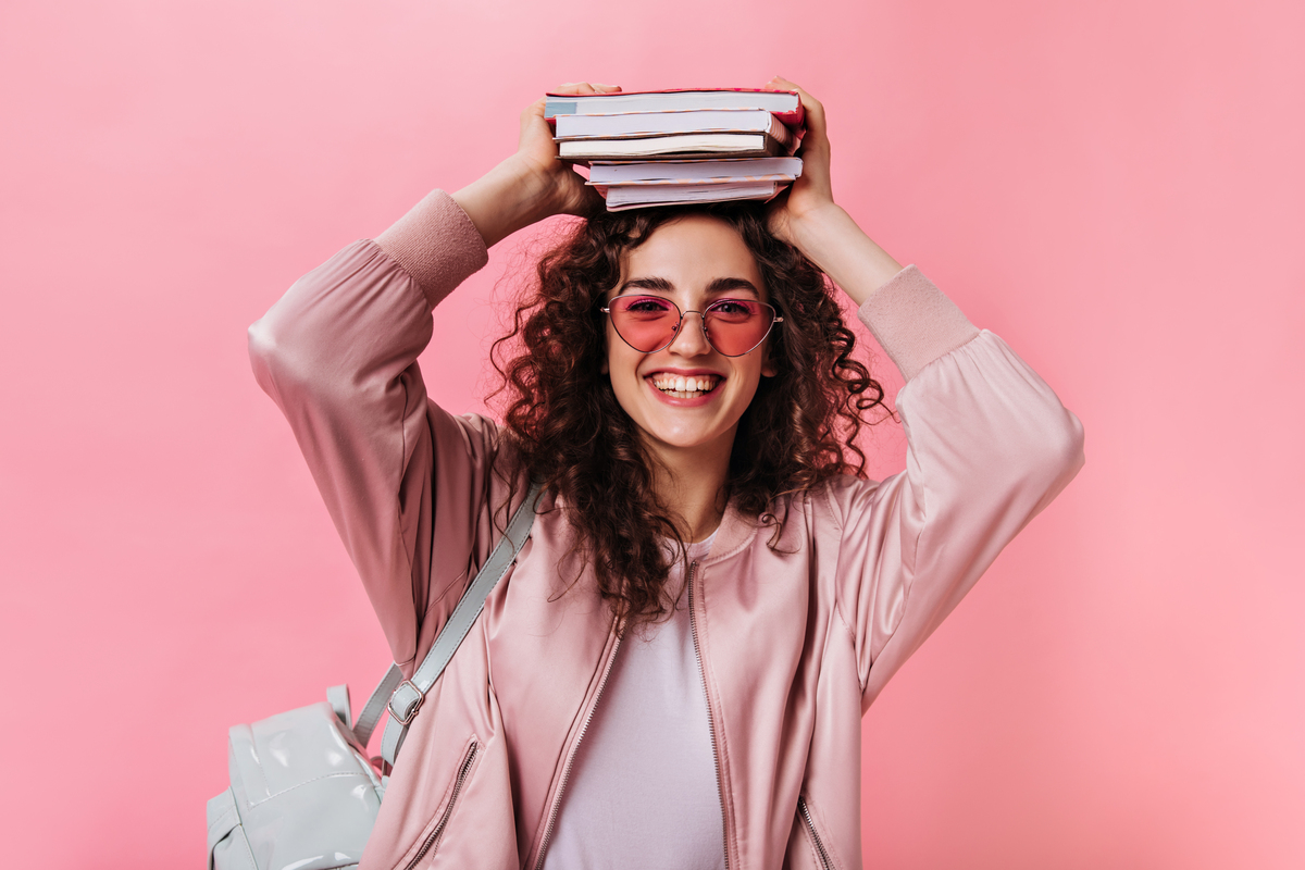 Adolescente en tenue rose posant avec des livres sur la tête