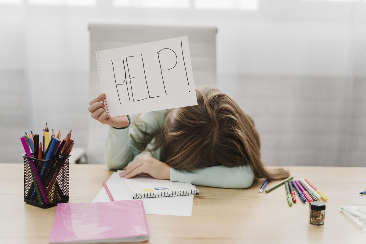 étudiante stressée qui est affalée sur le bureau avec une pancarte HELP