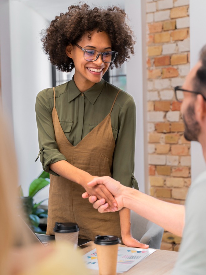 une commerçante coupe afro et un tablier marron qui serre la main à un client