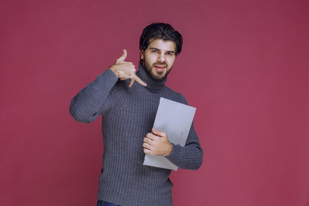 étudiant qui fait un geste de la main qui appelle sur fond rouge et qui tient un dossier dans les mains