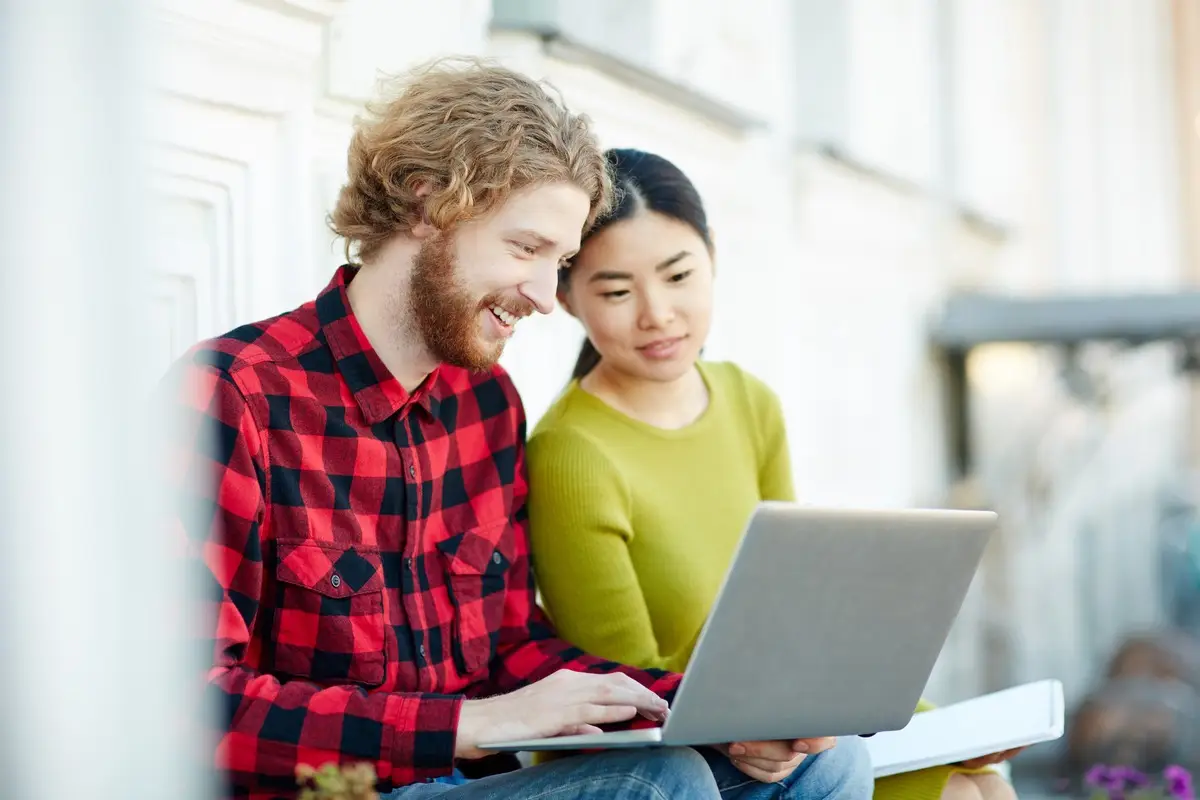 Two modern students with laptop working over college project outdoors